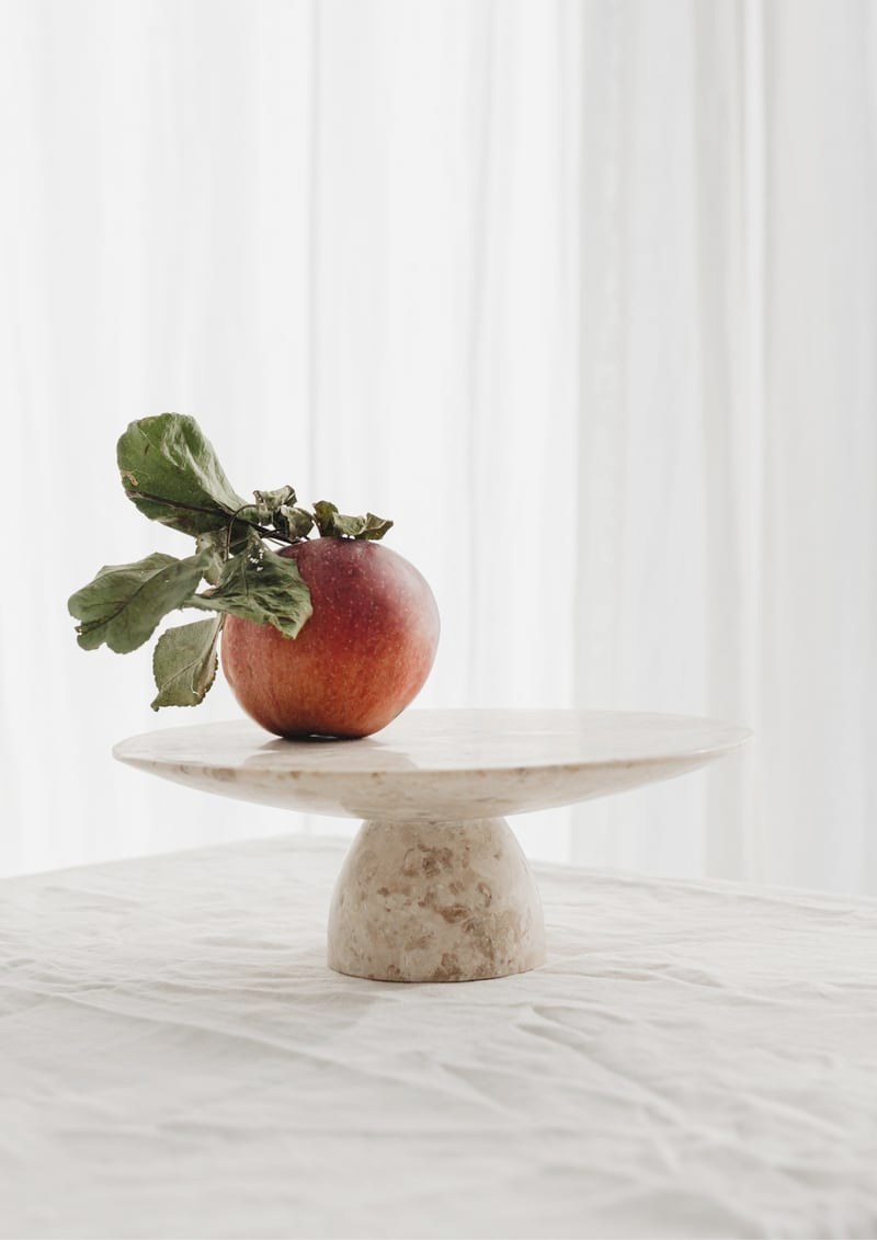 A still life of three stone and ceramic vessels on a pale plaster ledge in soft daylight