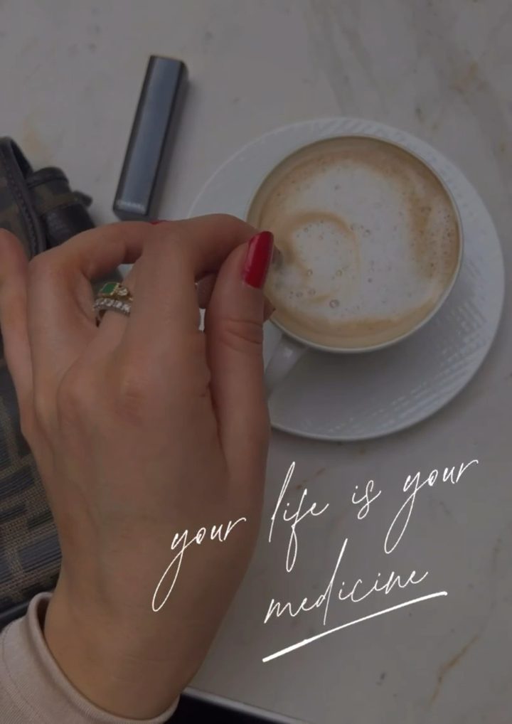 A hand with red nails lifting a cappuccino from a marble cafe table