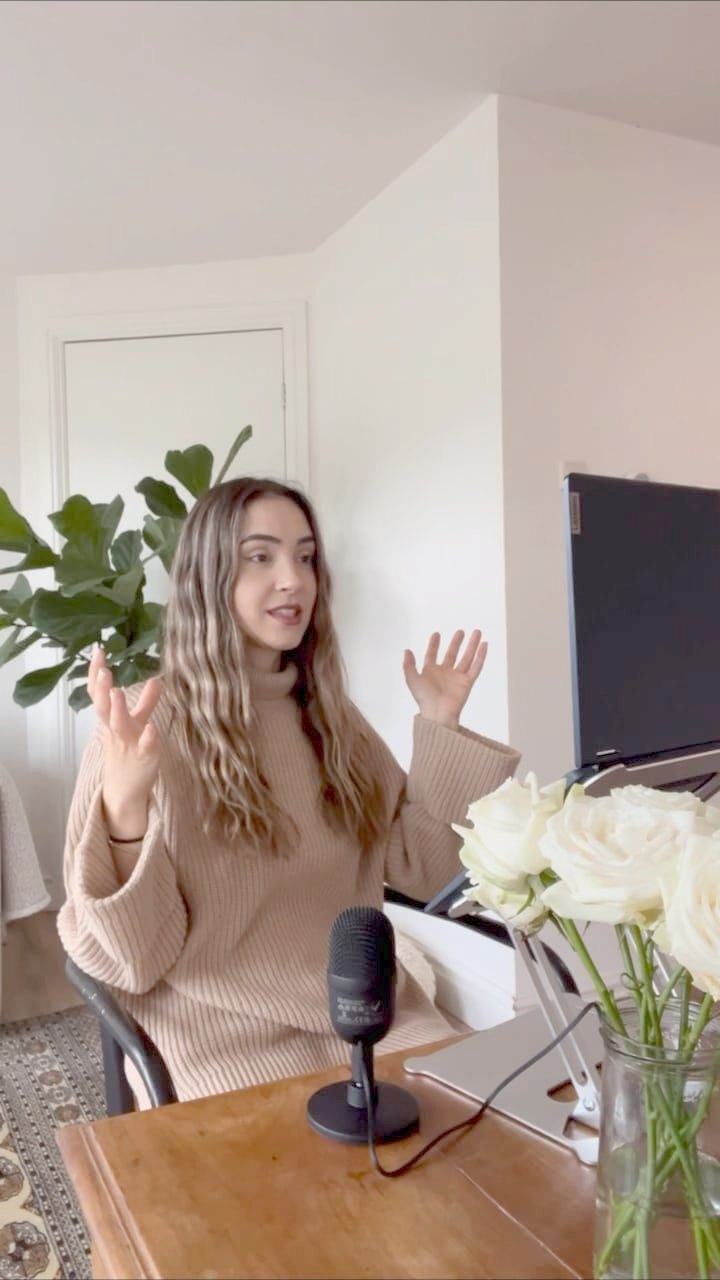 Gaye del Sol at a wooden desk speaking into a microphone, white roses beside her